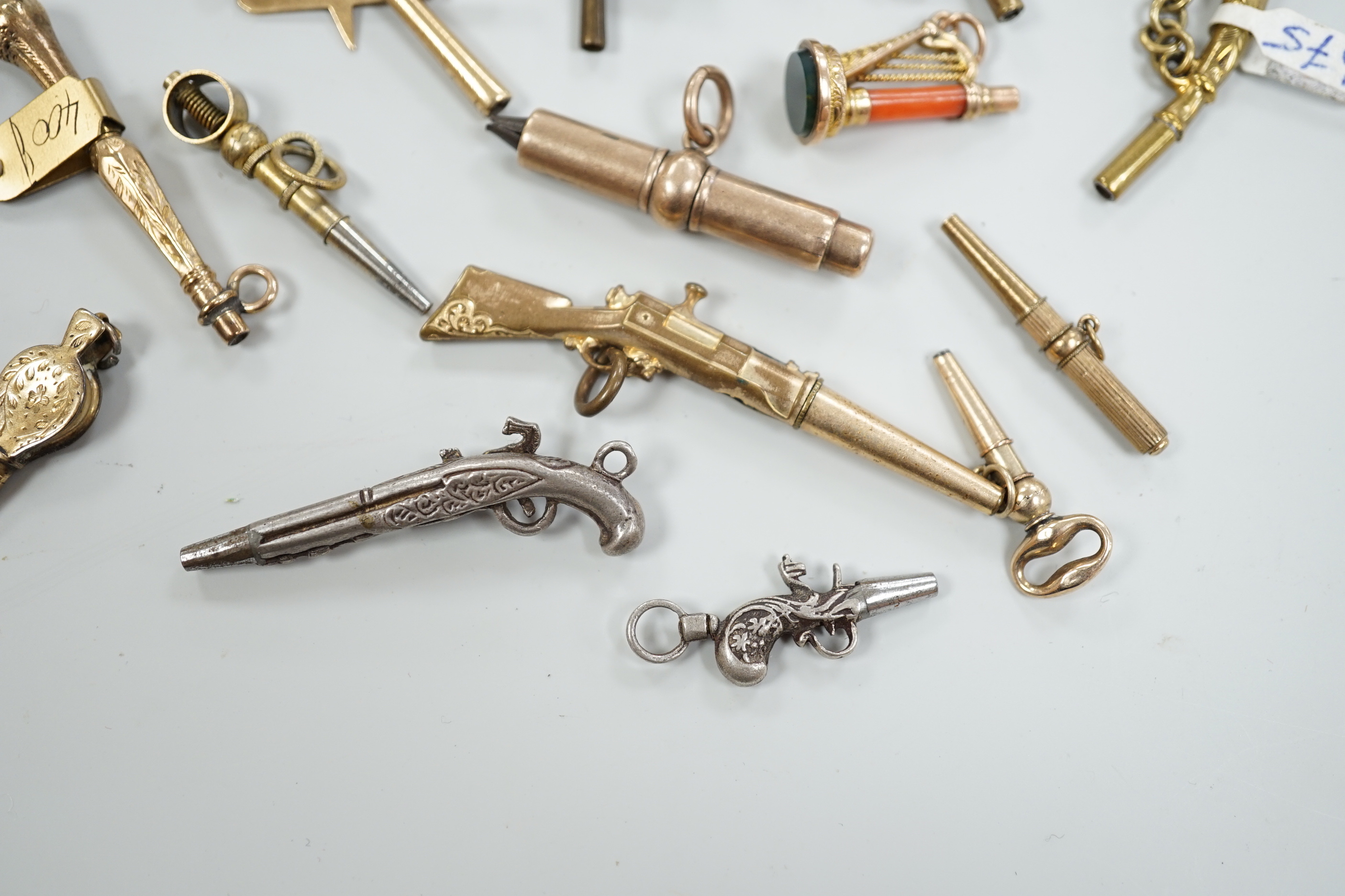 Eighteen assorted mainly 19th century base or yellow metal overlaid novelty watch keys, including coral and bloodstone set harp, pistol, rifle, cornucopia, bellows, horses hoof and trade insignia, largest 55mm.